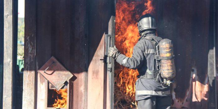 fire fighter in front of open door with flames behind it