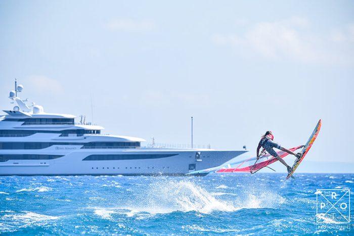 a windsurfer with a superyacht in the distance behind them